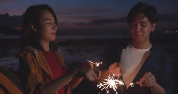 年轻的亚洲夫妇在夜间的海滩露营时 一边玩乐 一边用火花灯来庆祝 男女旅客在营地休息一下 户外活动 探险旅行或度假 — 图库视频影像