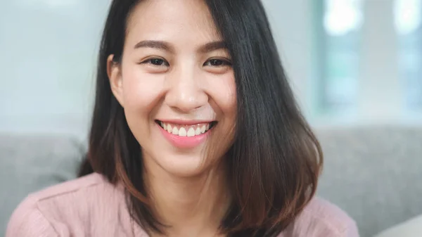 Teini-ikäinen aasialainen nainen hymyilee onnellisena ja etsii kameraa rentoutuessaan olohuoneessa kotona. Elämäntapa kaunis aasialainen nuori nainen käyttää rentoutumisaikaa kotona käsite. — kuvapankkivalokuva