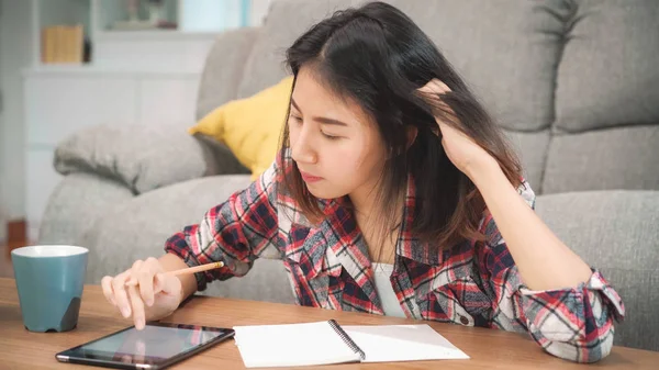 Mujer estudiante asiática hacer los deberes en casa, mujer beber café y el uso de la tableta para buscar en el sofá en la sala de estar en casa. Estilo de vida de las mujeres relajarse en el hogar concepto. — Foto de Stock