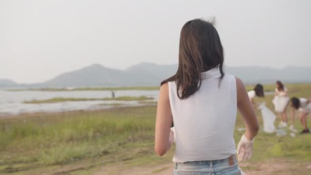 年轻的亚洲女性志愿者的肖像有助于保持自然的清洁 看着镜头 带着白色的垃圾袋在海滩上微笑 环境保护及污染问题的概念 — 图库视频影像