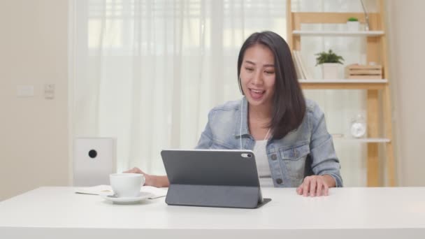 スローモーション フリーランスのビジネス女性が自宅のリビングルームでお客様とタブレットワーキングコールビデオ会議を使用してカジュアルウェア Happy若いですアジアの女の子リラックス座っています上のデスク仕事でインターネット — ストック動画