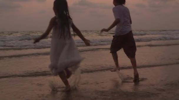Asiatique jeune famille heureuse profiter des vacances sur la plage en soirée. Papa, maman et enfant se détendent en courant dans la mer ensemble tandis que la silhouette coucher de soleil. Lifestyle Voyage vacances vacances concept d'été. 4k Mouvement lent .