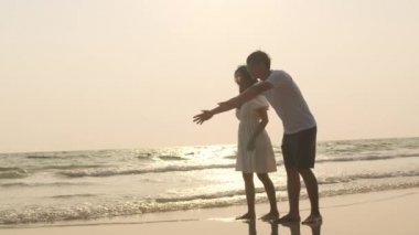 Asyalı genç mutlu aile akşamları sahilde tatilin tadını çıkarıyor. Baba, anne ve çocuk gün batımında deniz kenarında oynarken rahatlar. Hayat tarzı seyahat tatil yaz tatili konsepti. 4k ağır çekim.