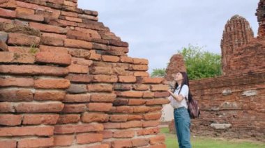 Gezgin Asyalı kadın fotoğraf çekmek için Ayutthaya, Tayland 'da tatil gezisi yaparken fotoğraf çekiyor. Japon bayan turist, geleneksel kentteki muhteşem şehir simgesinde yolculuğunun tadını çıkarıyor. Yavaş çekim.