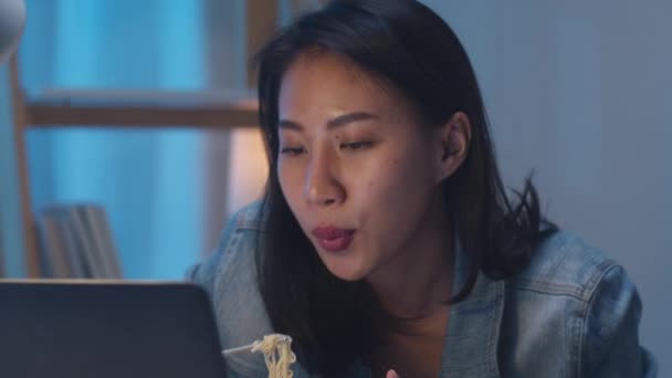 亚洲自由职业聪明的商业女性在晚上在客厅的笔记本电脑上工作的同时 还在吃方便面 快乐的年轻亚洲女孩坐在办公桌前加班 享受放松的时光 — 图库视频影像