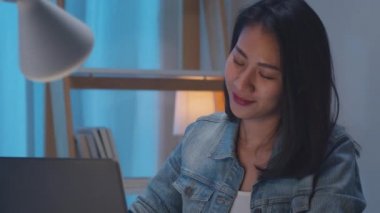Ağır çekim - Serbest çalışan zeki iş kadınları dizüstü bilgisayar kullandıktan sonra müzik dinliyorlar geceleri evde sıkı çalışıyorlar. Mutlu genç Asyalı kız masa başında fazla mesai yapıyor, dans ediyor, dinleniyor..