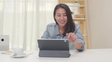 Asya 'nın serbest ve zeki iş kadınlarının portresi evde çalışma odasındaki iş yerinde tablet kullanarak günlük giyim kuşamı. Mutlu Asyalı genç kız, rahat ol masa başında otur ve internette işini yap..