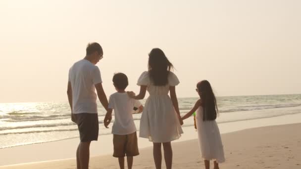 アジアの若い幸せな家族は夕方にビーチで休暇を楽しむ お父さん お母さん 子供たちは日没時に一緒に海の近くを歩いてリラックスします ライフスタイル旅行休暇夏旅行のコンセプト 4Kスローモーション — ストック動画