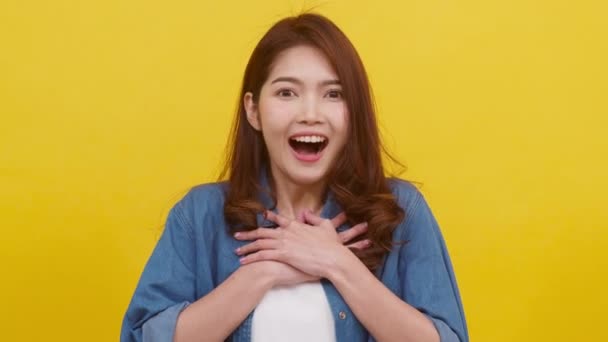 カジュアルな布に身を包み 黄色を背景にカメラを見る ポジティブな表情 楽しさと刺激的な肖像画の若いアジアの女性 幸せな愛らしい幸せな女性は成功を喜びます スローモーション — ストック動画