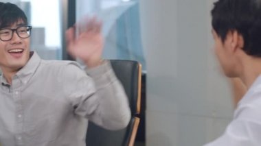 Asya 'lı genç iş adamları akıllı gündelik kıyafetlerle iş arkadaşlarını yumrukluyor başarılı takım çalışmasını kutluyorlar mutlu iş arkadaşlarıyla motive oluyorlar iyi iş çıkarmanın sonucu olarak ofisdeki toplantı odasında tebrik ediyorlar..