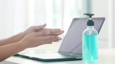 Koronavirüsü korumak için laptoptan önce el dezenfektanı kullanan Asyalı bir kadın. Kadın, sosyal uzaklık evde kaldığında ve kendini karantinaya aldığında, alkolü temizlik için zorlar.