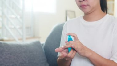 Koronavirüsü korumak için el dezenfektanı kullanan Asyalı bir kadın. Sosyal uzaklık evde kalıp kendini karantinaya alırken, bir kadın temiz bir el ile kanepeye oturuyor..
