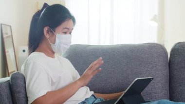 Asyalı serbest çalışan kadın günlük kıyafet tablet çalışma video konferansı kullanarak evden oturma odasına müşteri çağırma sosyal uzaklık evde ve kendi kendine karantina zaman.