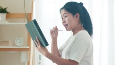Asyalı serbest çalışan kadın günlük kıyafet tablet çalışma video konferansı kullanarak evden oturma odasına müşteri çağırma sosyal uzaklık evde ve kendi kendine karantina zaman.