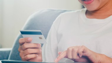 Sosyal uzaklık evde kalırken ve kendini karantina süresi, online alışveriş, koronavirüs konsepti kullanırken, Asyalı kadın tablet, kredi kartı satın alıp evden e-ticaret interneti satın alıyor..