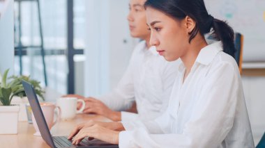 Başarılı güzel yönetici Asya 'lı genç iş kadını modern ofis işyerinde çalışırken dizüstü bilgisayarda yaratıcı fikirler hakkında özel ders izleyerek gündelik giyiniyor..