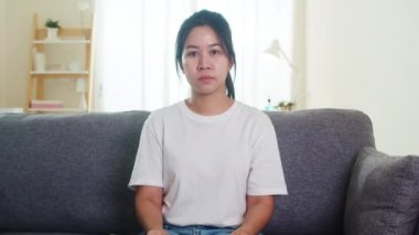 İç karartıcı Asyalı iş kadını koruyucu maske takıyor oturma odasındaki koltukta oturuyor sosyal mesafeler evde ve karantinada kalırken, Çin 'de salgın hastalık, koronavirüs konsepti.