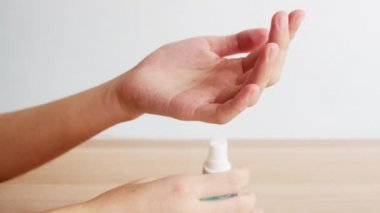 Koronavirüsü korumak için el dezenfektanı kullanan Asyalı bir kadın. Kadın, sosyal uzaklık evde kalıp kendini karantinaya alırken alkol şişesini hijyen için temizlemeye zorlar..