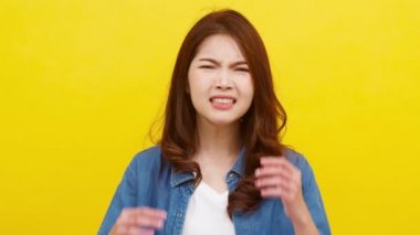 Olumsuz ifadeli genç Asyalı bir kadının portresi. Heyecanlı çığlık çığlığa ağlayan, günlük kıyafetlerle öfkeli ve sarı arka plandaki kameraya bakan. Yüz ifadesi kavramı. 