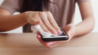 Koronavirüsü korumak için kullanmadan önce cep telefonuna alkol spreyi sıkan Asyalı bir kadın. Sosyal uzaklık evde kaldığında ve kendini karantinaya aldığında hijyen için kadın temiz yüzey.