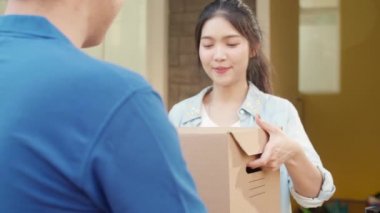 Genç posta kuryesi, paketleri müşteriye göndermek için elinde tutuyor. Asyalı kadınlar, açık hava paketleri almak için cep telefonlarında QR kodu ile imza atıyor ve ödeme yapıyorlar..