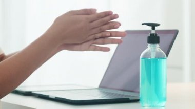 Koronavirüsü korumak için laptoptan önce el dezenfektanı kullanan Asyalı bir kadın. Kadın, sosyal uzaklık evde kaldığında ve kendini karantinaya aldığında, alkolü temizlik için zorlar.