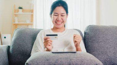 Sosyal uzaklık evde kalırken ve kendini karantina süresi, online alışveriş, koronavirüs konsepti kullanırken, Asyalı kadın tablet, kredi kartı satın alıp evden e-ticaret interneti satın alıyor..