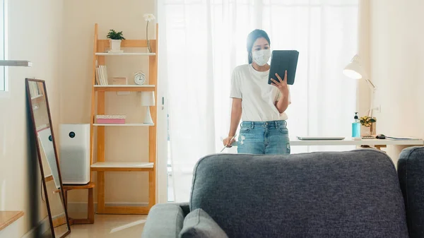 Asian business woman wearing mask using tablet working call video conference with customer in living room from home when social distancing stay at home and self quarantine time, coronavirus concept.