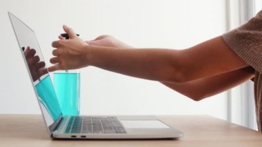Koronavirüsü korumak için laptopta çalışırken alkol jeli kullanan Asyalı kadın. Kadın, sosyal uzaklık evde kaldığında ve kendini karantinaya aldığında, alkolü temizlik için zorlar..