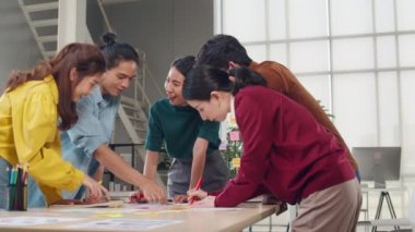 Asyalı iş adamları ve iş kadınları yaratıcı web tasarım uygulaması hakkında fikir alışverişinde bulunuyorlar ve cep telefonu projesinde birlikte çalışmak için şablon planı geliştiriyorlar. Yavaş çekim.
