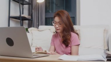 Genç Asya 'lı genç kız öğrenci uzaklık dersini çevrimiçi öğretmenle birlikte öğreniyor ve geceleri evden oturma odasına bilgisayarda çalışıyor. Corona virüsünün önlenmesi için sosyal mesafe ve karantina.