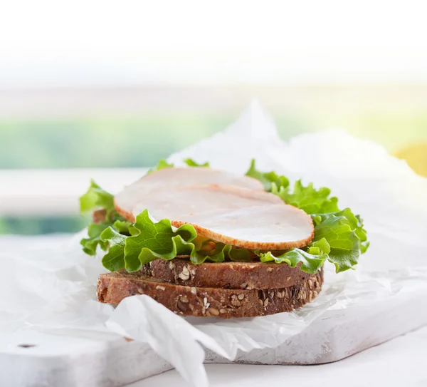 Hausgemachtes leckeres Sandwich mit Salatblättern und Schinken auf einem Schneidebrett auf Küchenhintergrund, horizontal mit Platz für Text — Stockfoto