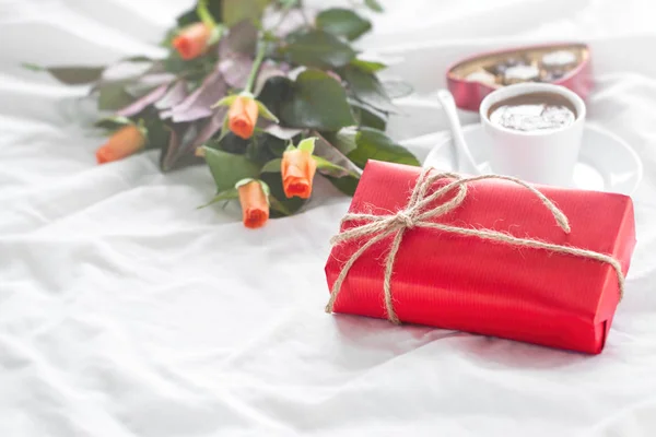 美しいカラフルなギフトやベッドの上にチョコレートのプラリネ、コーヒーや新鮮なバラと自然紙の中に存在します。休日、バレンタインデーまたは驚きのコンセプト — ストック写真