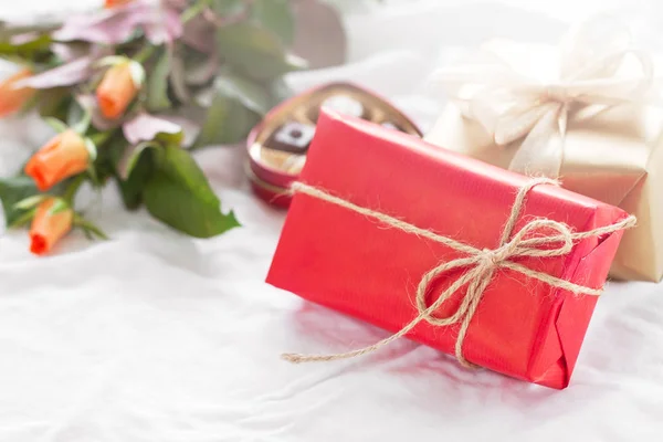 Hermoso regalo colorido bonito o presente en un papel natural con pralinés de chocolate, café y rosas frescas en una cama —  Fotos de Stock
