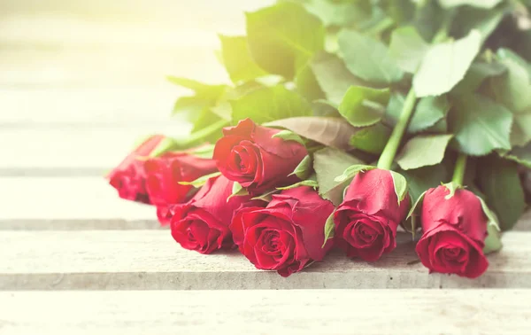 Hermosas rosas rojas sobre un fondo de madera con hermosa luz — Foto de Stock