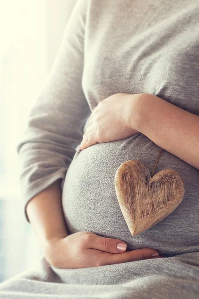 Νεαρή έγκυος γυναίκα κατέχει ξύλινη καρδιά. Έννοια της αγάπης. Παστέλ σε — Φωτογραφία Αρχείου