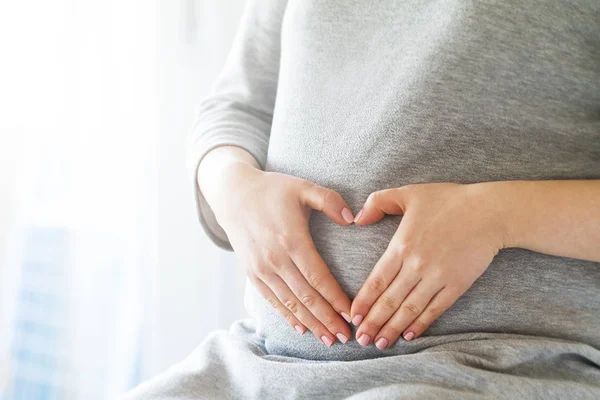 Gravid kvinna som håller händerna på hennes svullna magen forma en — Stockfoto