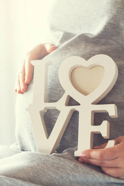 Unga gravid kvinna håller trä bokstäver kärlek. Kärlek-konceptet. — Stockfoto