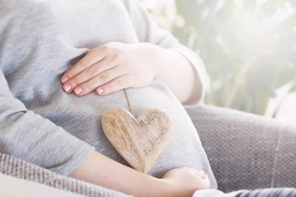 Ung gravid kvinna håller trä hjärta. Kärlek koncept. — Stockfoto