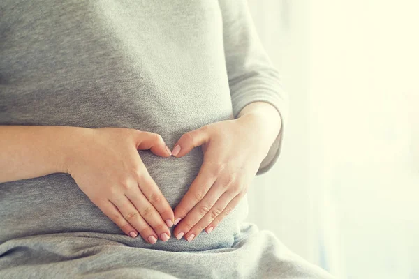 Pregnant woman holding her hands on her swollen belly — Stock Photo, Image