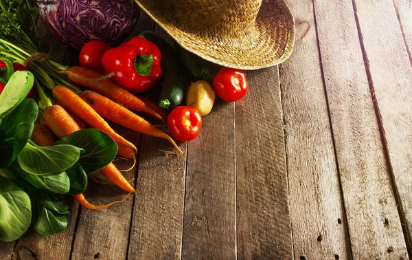 Beautiful fresh harvest vegetables on wooden table with straw hat — Stock Photo, Image