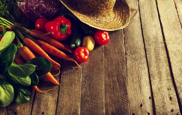 Beautiful fresh harvest vegetables on wooden table with straw hat — Stock Photo, Image