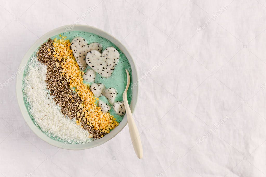 tasty smoothie bowl with yogurt, coconut flakes, chia seeds, dragon fruit pieces and spirulina on textile background