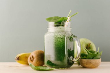green refreshing smoothie drink in glass jar with ingredients on table clipart