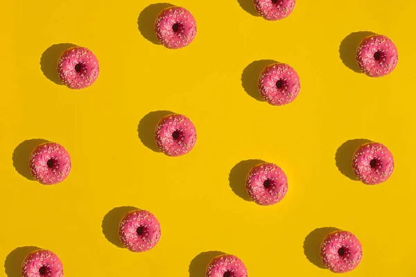 Плоская Укладка Повторяющихся Розовых Глазированных Пончиков Брызгами Ярко Желтом Фоне — стоковое фото
