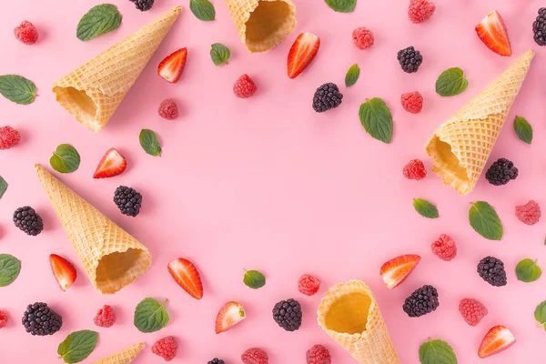 empty waffle cones with mixed berries and mint leaves on pink background