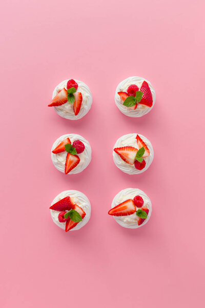  подают кусочки безе с клубничными ломтиками на розовой поверхности
