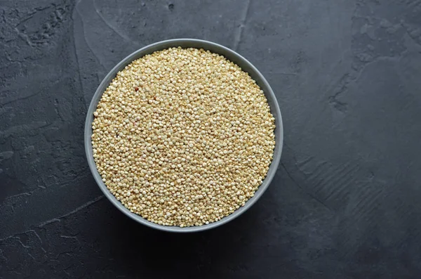 Dry organic quinoa seeds in gray ceramic bowl on dark concrete background — Stock Photo, Image