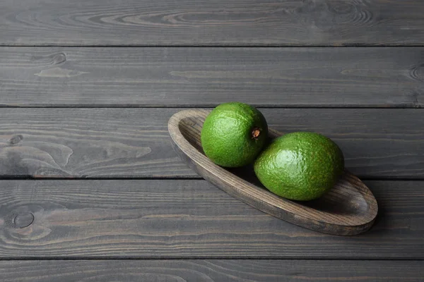 Frische Bio-Avocado in Holzteller auf dunklem Holztischhintergrund, Ansicht von oben — Stockfoto