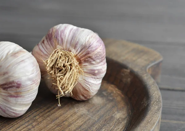 Dry garlic bulbs in wooden plate on old dark wooden background — Stock Photo, Image